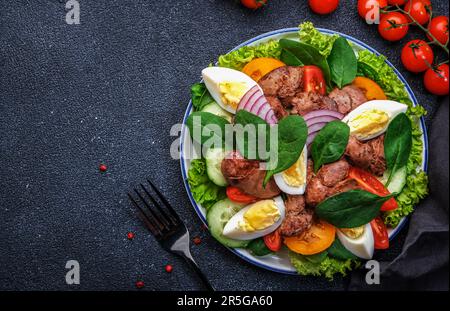 Salade Périgord avec foie de poulet rôti, tomates rouges, concombres, œufs durs, laitue et épinards. Arrière-plan de la table de cuisine noire, vue du dessus Banque D'Images