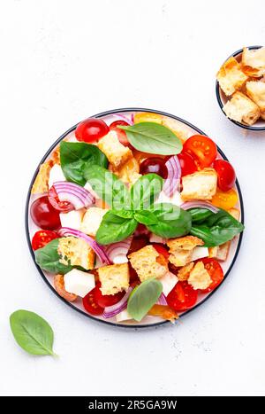 Panzanella salade de légumes italiens avec pain rassis, tomates colorées, fromage mozzarella, oignon, huile d'olive, sel et basilic vert, fond de table blanc Banque D'Images