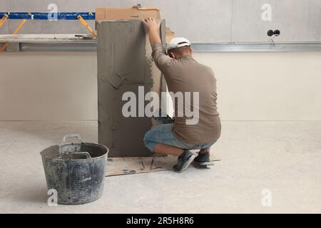 Le travailleur répartissant le mélange d'adhésif sur les carreaux avec une spatule Banque D'Images