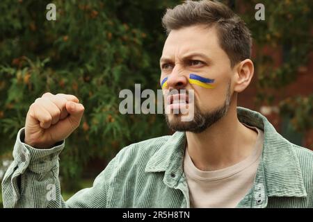 Homme en colère avec des dessins de drapeau ukrainien sur le visage à l'extérieur Banque D'Images