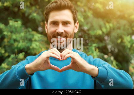 Homme heureux faisant des gestes de coeur en plein air, se concentrer sur les mains Banque D'Images