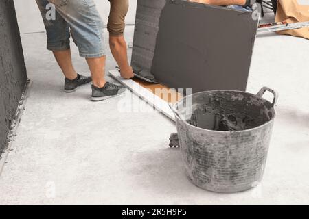 L'employé répandant le mélange d'adhésif sur les carreaux avec une spatule, gros plan Banque D'Images