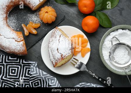 Morceau de délicieux gâteau au yaourt maison avec sucre en poudre et mandarines sur table grise, plat Banque D'Images