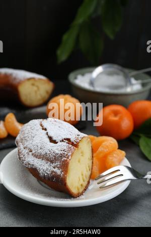 Morceau de délicieux gâteau au yaourt maison avec sucre en poudre et mandarines sur table grise Banque D'Images