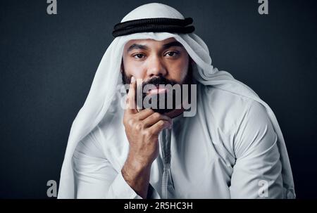 HES tout sur la tradition et les affaires. Photo en studio d'un jeune homme vêtu de vêtements traditionnels islamiques se posant sur un fond sombre. Banque D'Images