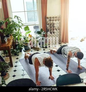 Chaque jour devrait être le jour de yoga. deux jeunes hommes qui font des planches pendant une routine de yoga à la maison. Banque D'Images