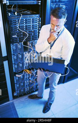 Il doit y avoir une sorte d'erreur ici... une photo en grand angle d'un homme mûr utilisant un ordinateur portable tout en travaillant dans une salle de serveurs. Banque D'Images
