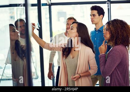 Travailler sur un autre plan ambitieux et audacieux. un groupe de jeunes designers remue-méninges avec des notes sur un mur de verre dans un bureau. Banque D'Images
