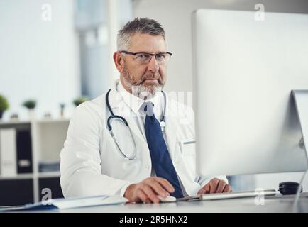 Rester informé des progrès réalisés dans le domaine médical. Portrait d'un médecin mature utilisant un ordinateur à un bureau dans son bureau. Banque D'Images