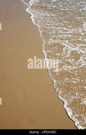 Une petite vague roule sur une belle plage de sable. Banque D'Images