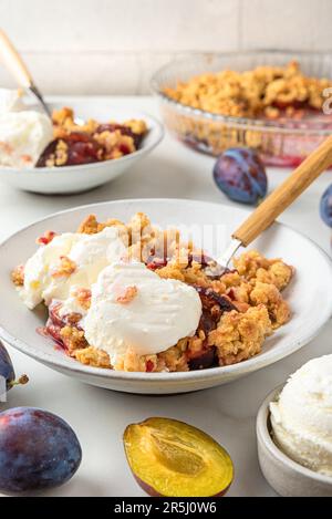 Crumble aux fruits. Tarte aux prunes avec glace à la vanille dans des assiettes avec des cuillères sur une table en marbre blanc pour un petit déjeuner savoureux Banque D'Images