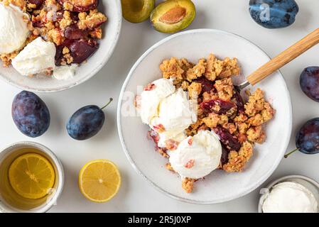 Tarte aux prunes avec glace à la vanille dans des assiettes et une tasse de thé sur une table en marbre blanc pour un délicieux petit déjeuner Banque D'Images