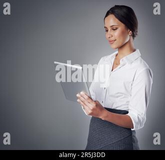 Rester compétitif grâce à une technologie de pointe. Photo en studio d'une jeune femme d'affaires utilisant une tablette numérique contre un gris Banque D'Images