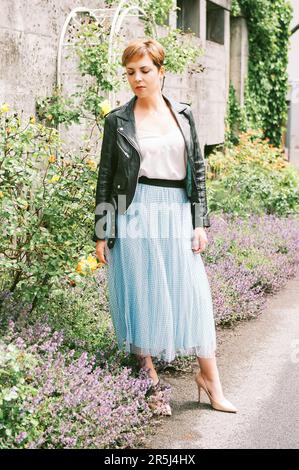 Portrait extérieur de la belle femme mûre portant une jupe bleue et une veste en cuir noir Banque D'Images