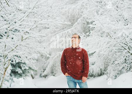 Portrait extérieur de l'âge moyen 55 - 60 ans homme appréciant le beau temps froid dans la forêt d'hiver, portant le pull-over rouge tricoté Banque D'Images