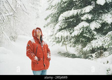 Portrait extérieur d'un homme d'âge moyen qui profite d'une belle journée en forêt d'hiver, qui marche sous la neige, portant une veste rouge orange Banque D'Images