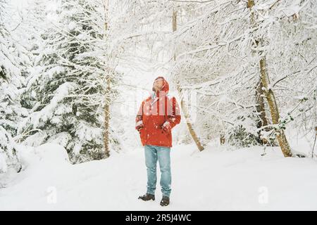 Portrait extérieur d'un homme d'âge moyen qui profite d'une belle journée en forêt d'hiver, qui marche sous la neige, portant une veste rouge orange Banque D'Images