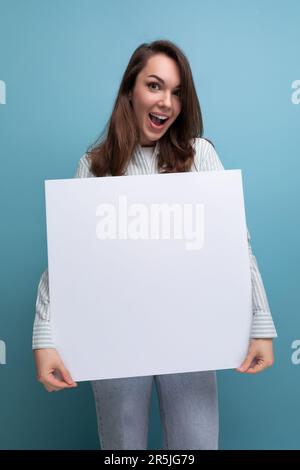 adorable femme brune de 25 ans dans une chemise et un jean démontre un projet sur une maquette de feuille blanche Banque D'Images
