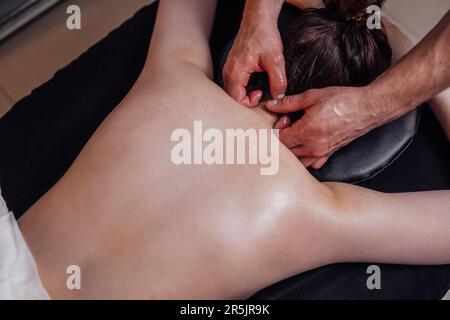 Bonne jeune fille caucasienne se massant de dos dans le salon de spa. Mains propres de masseuse masculine. Belle femme souriante obtient la détente. Copier l'espace. Banque D'Images