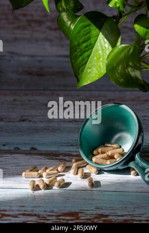 Un petit bol en céramique contenant des capsules de supplément alimentaire sur un fond en bois et quelques feuilles Banque D'Images