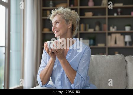 Bonne femme rêveuse senior tenant une tasse de boisson chaude Banque D'Images