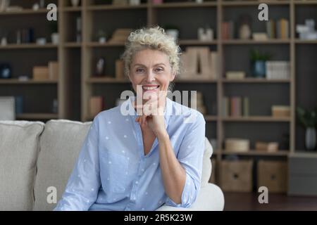Positive belle femme blonde mûre posant pour tirer sur le canapé Banque D'Images