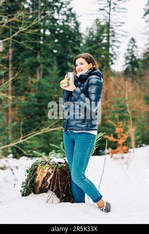 Portrait en plein air d'une belle jeune femme qui profite d'une belle journée dans la forêt, en tenant des thermos avec une boisson chaude Banque D'Images