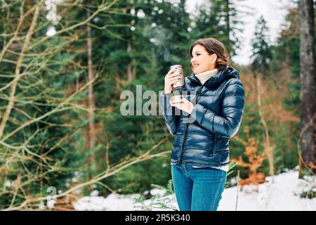 Portrait en plein air d'une belle jeune femme qui profite d'une belle journée dans la forêt, en tenant des thermos avec une boisson chaude Banque D'Images