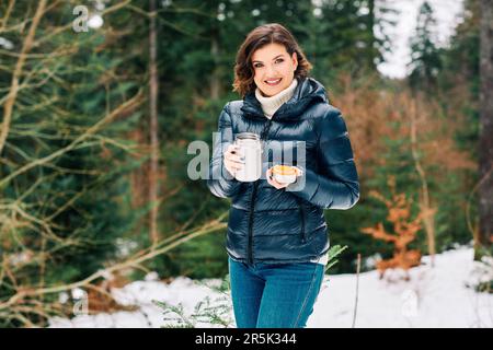 Portrait en plein air d'une belle jeune femme qui profite d'une belle journée dans la forêt, en tenant des thermos avec une boisson chaude Banque D'Images