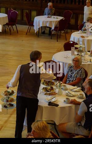 Un serveur mâle sert des plats salés et des gâteaux sur deux plateaux à trois niveaux aux clients du Royal Hall, Harrogate, North Yorkshire, Angleterre, Royaume-Uni. Banque D'Images