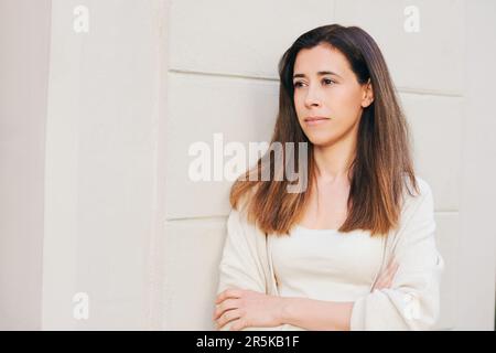 Portrait extérieur de la belle femme hispanique penchée sur le mur, portant des vêtements beiges Banque D'Images