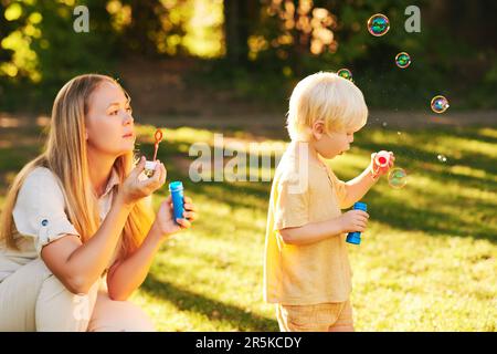 Bonne jeune mère et adorable jeune garçon jouant avec des bulles de savon dans le parc d'été, bonne enfance Banque D'Images