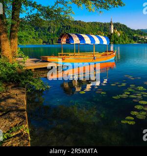 Bateau de pletna ancré à la jetée sur le lac. Bateau à rames et célèbre église en arrière-plan sur la petite île, Bled, Slovénie, Europe Banque D'Images