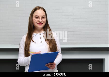 Portrait confiant d'une jeune femme, réceptionniste avec presse-papiers près du bureau dans une clinique moderne, souriant regardant la caméra Banque D'Images