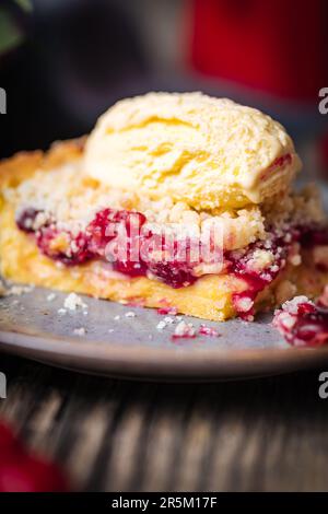 Tarte à la crème de cerise aigre, pâtisserie à la crème et miettes, servie avec de la crème glacée à la vanille. Ambiance et décoration rustiques et moody. Banque D'Images