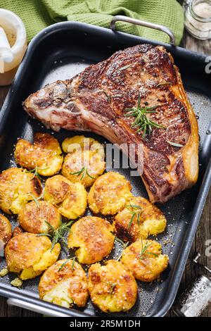 Première coupe de steak avec pommes de terre cuites au four servi dans un plateau en métal Assaisonné de romarin, de poivre et d'ail. Steak de Ribeye juteux et délicieux Banque D'Images