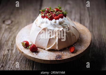 Gâteau Pavlova décoré de fraises sur une table rustique en bois. Le gâteau est fait de meringue et de crème fouettée Banque D'Images