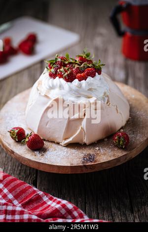 Gâteau Pavlova décoré de fraises sur une table rustique en bois. Le gâteau est fait de meringue et de crème fouettée Banque D'Images