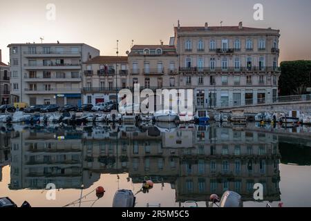 Sète, France. 26th mai 2023. Les bâtiments se reflètent dans l'eau calme du canal principal de Sète. La ville autrefois classe ouvrière de Sète, avec ses chantiers navals et son industrie de la pêche, est en train d'être transformée en une destination touristique de premier plan. La gentrification est accélérée par la colonisation des travailleurs nomades et des artistes, qui font monter les prix de l'immobilier. Crédit : SOPA Images Limited/Alamy Live News Banque D'Images