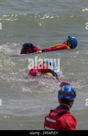 Affichage conjoint des services d'urgence axé sur la sécurité de l'eau. Les équipages et les navires de RNLI et de Coastguard démontrent le rétablissement d'une victime de la mer. Banque D'Images