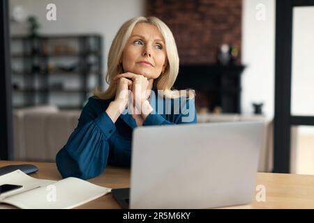 Femme d'affaires rêveuse et mûre pensant à quelque chose, travaillant sur un ordinateur portable et regardant loin, l'espace de copie Banque D'Images