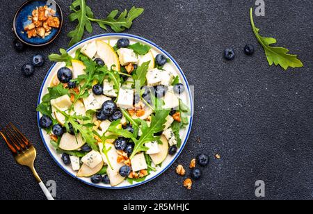 Salade gastronomique aux poires sucrées, aux bleuets, au fromage bleu, à l'arugula et aux noix. Arrière-plan de table noir, vue du dessus Banque D'Images