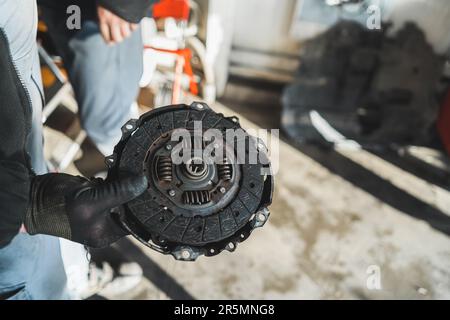 Mains de mécanicien tenant un ancien embrayage cassé à l'atelier de réparation automobile. Photo de haute qualité Banque D'Images