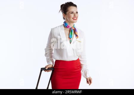 femme élégante et souriante de la compagnie aérienne sur fond blanc en uniforme avec un sac de voyage regardant au loin. Banque D'Images