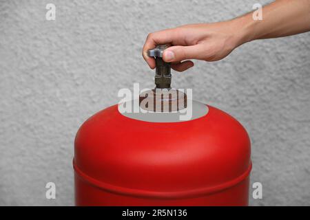 Homme ouvrant la bouteille de gaz rouge près du mur, gros plan Banque D'Images