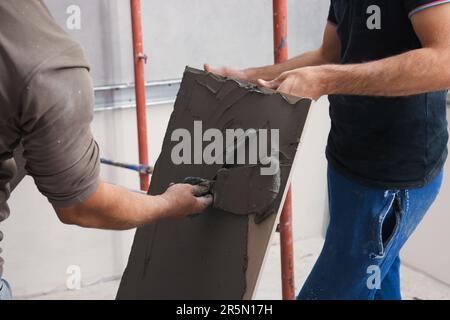L'employé répandant le mélange d'adhésif sur les carreaux avec une spatule, gros plan Banque D'Images