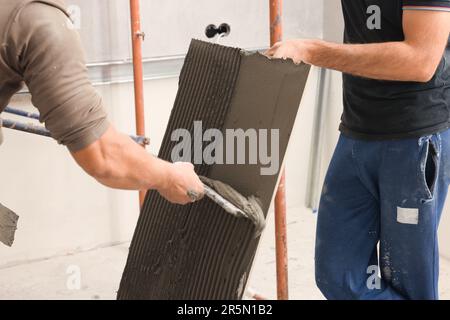 L'employé répandant le mélange d'adhésif sur les carreaux avec une spatule, gros plan Banque D'Images
