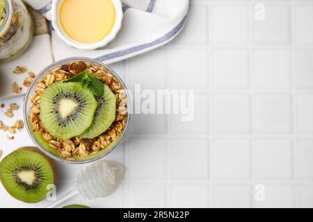 Délicieux dessert avec kiwi, muesli et fruits frais coupés sur table blanche, plat. Espace pour le texte Banque D'Images