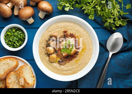 Délicieuse soupe à la crème de champignons et ingrédients sur une table en bois bleu, plat Banque D'Images