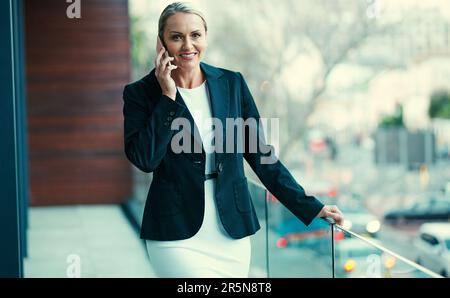 Toujours bon d'entendre un client heureux. Portrait d'une femme d'affaires mature debout à l'extérieur sur le balcon d'un bureau et utilisant un téléphone portable. Banque D'Images